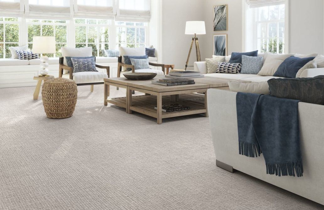 A cheerful family of four sits on plush, beige carpet flooring in a sunlit living room of an Indianapolis home. A golden retriever sits happily in the center as the children pet and play with it, while the parents smile and laugh from the nearby sofa. The