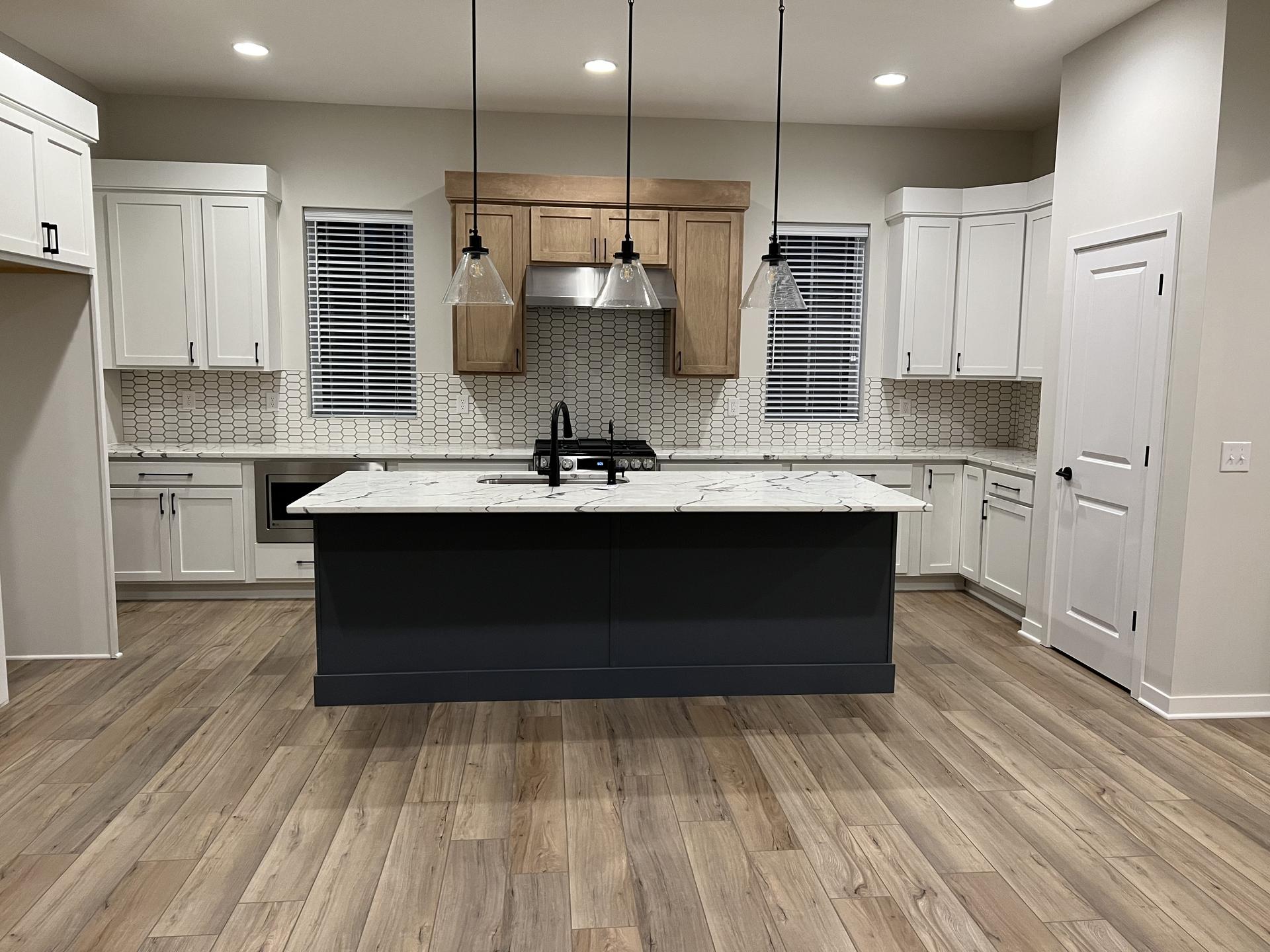 Waterproof wood-look flooring in a modern Indianapolis kitchen featuring wide plank warm neutral tones, white shaker cabinets, a black island with quartz countertop, pendant lighting, and a clean, open layout designed for durability and everyday use.